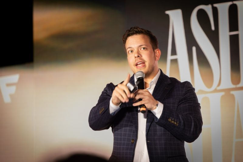 Ashton Shanks speaking on stage to a room of agency owners in 2023.